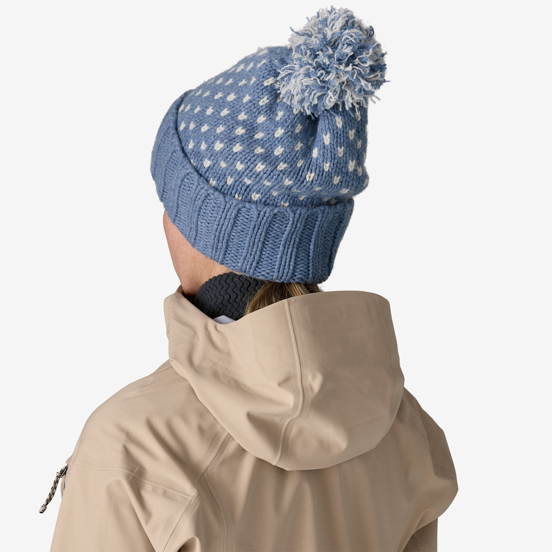 Person wearing a blue knit beanie with a pom-pom and beige jacket on a white background