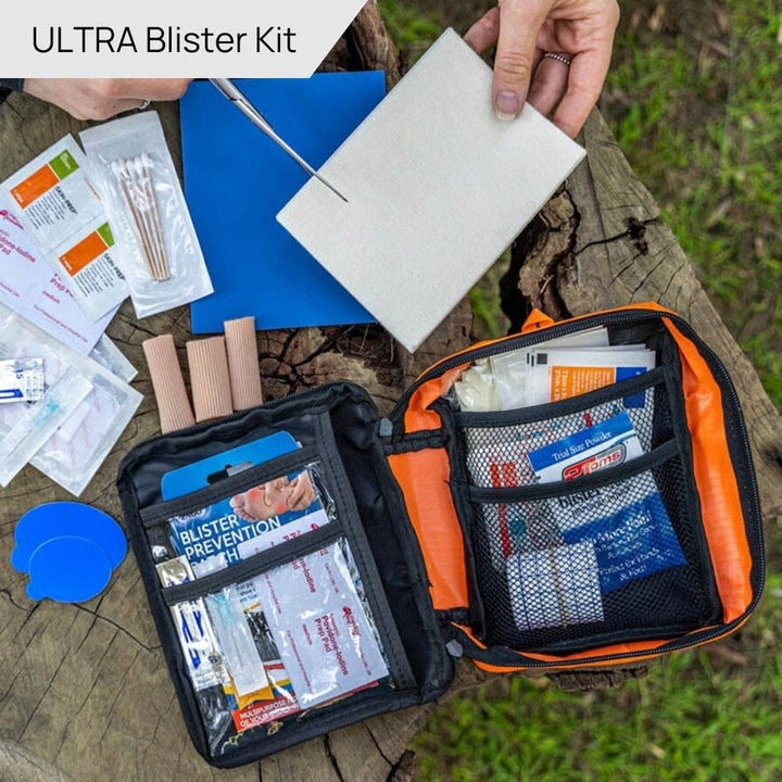 Orange and black first aid kit with contents spread out on a stump