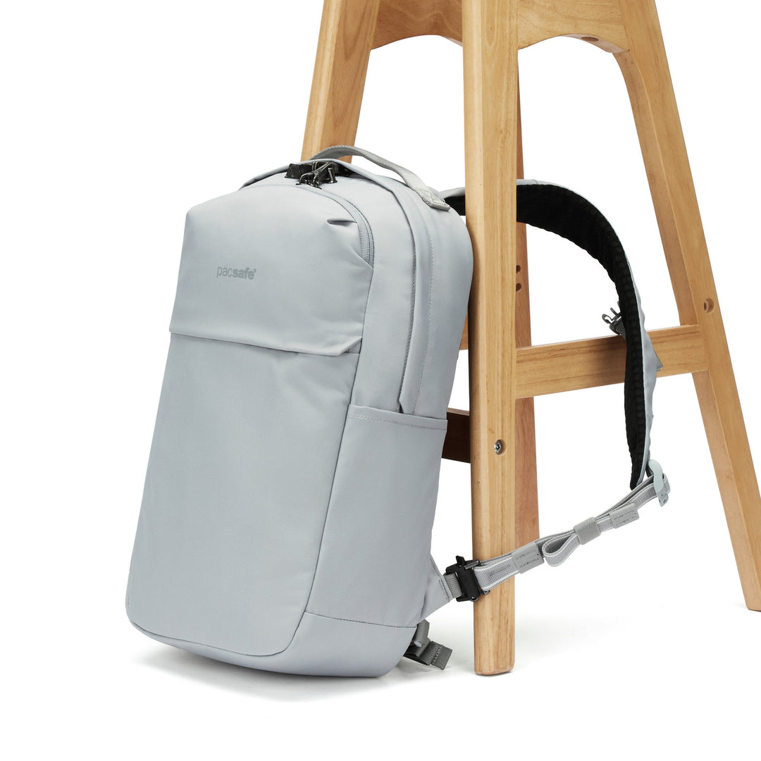 Grey backpack leaning against a wooden stool with shoulder strap clipped though one leg