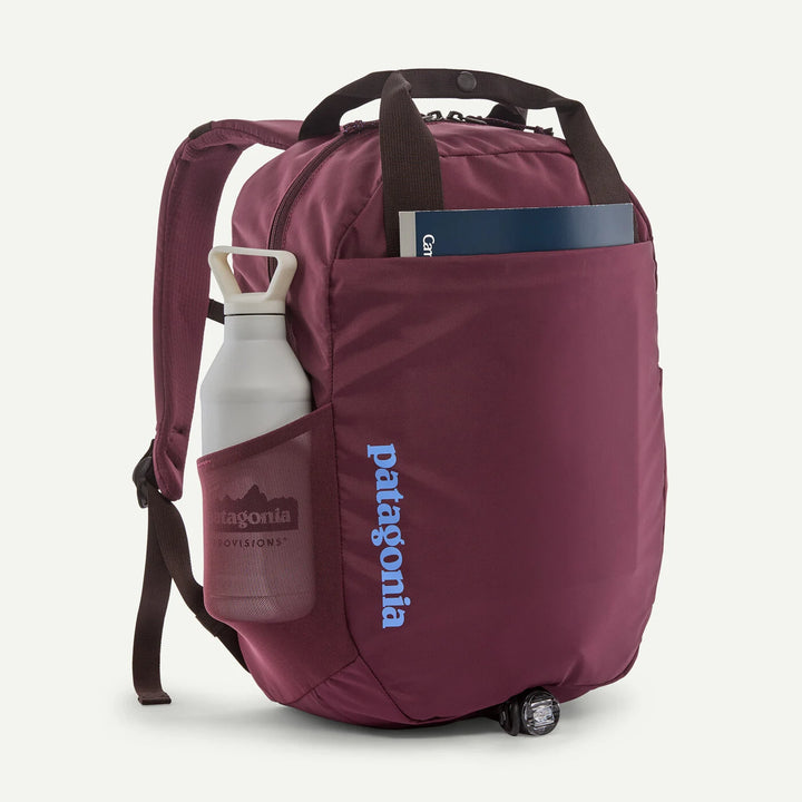 A Patagonia backpack in burgundy with a blue vertical logo, shown on a white background with a white water bottle in its side pocket and a book in the top pocket.