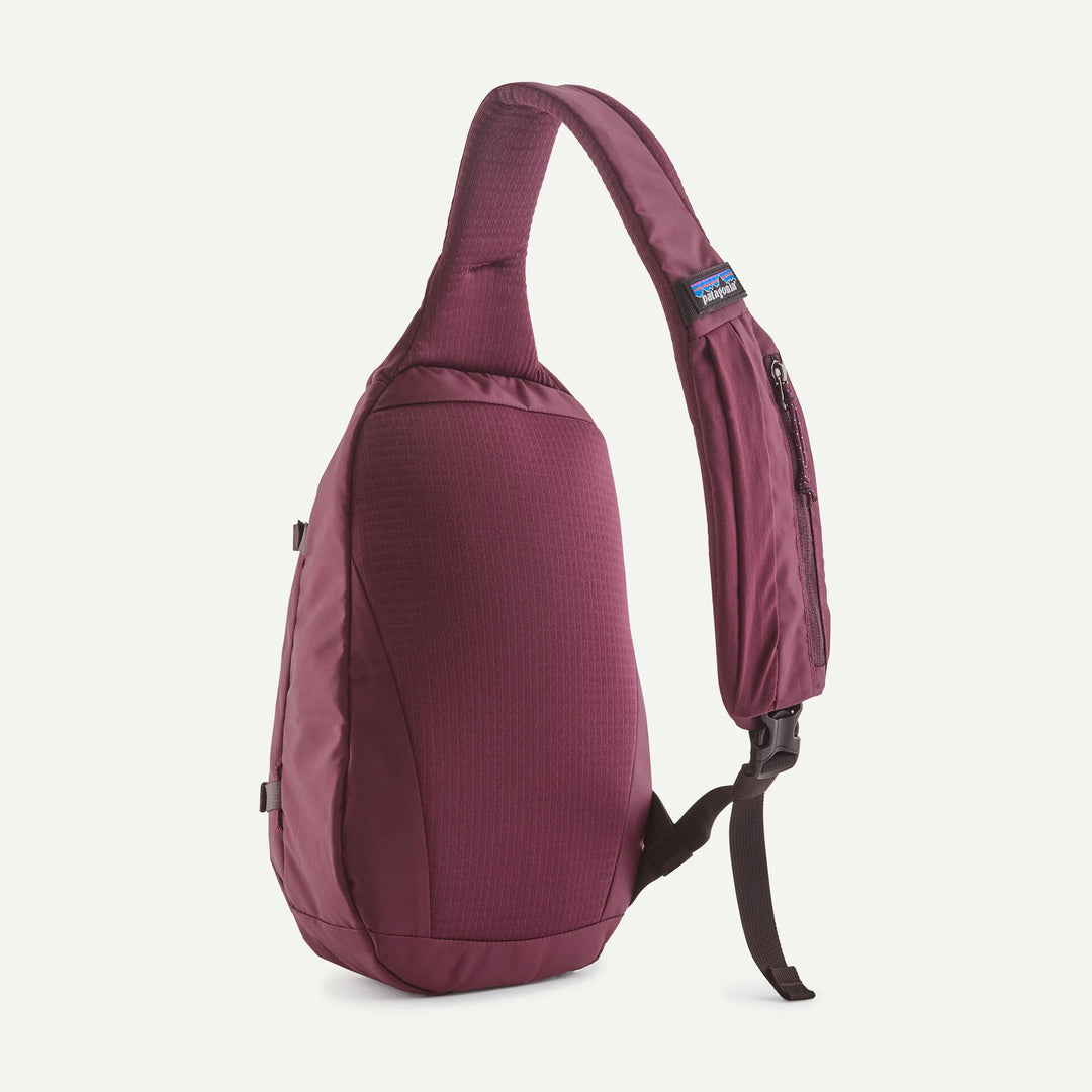 A single-strap sling backpack in a textured burgundy fabric, shown from a side profile view against a clean off-white background. A small blue and white Patagonia logo patch is visible on the upper strap.