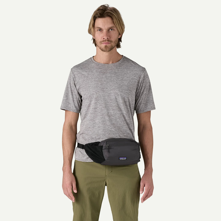 Man wearing a gray t-shirt and green pants with a black waist bag on a white background