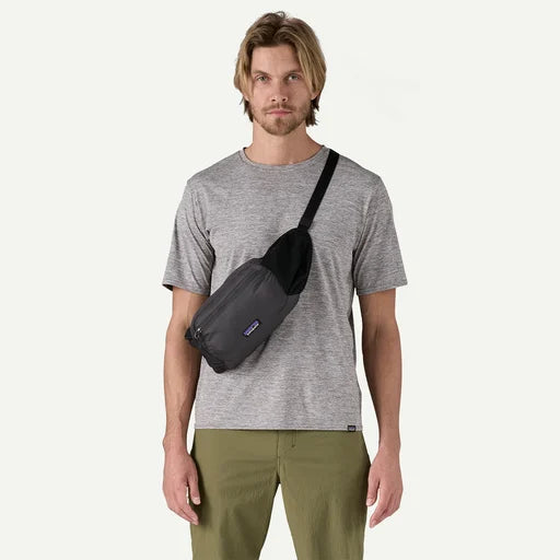 Man wearing a gray t-shirt and green pants with a black sling bag on a white background