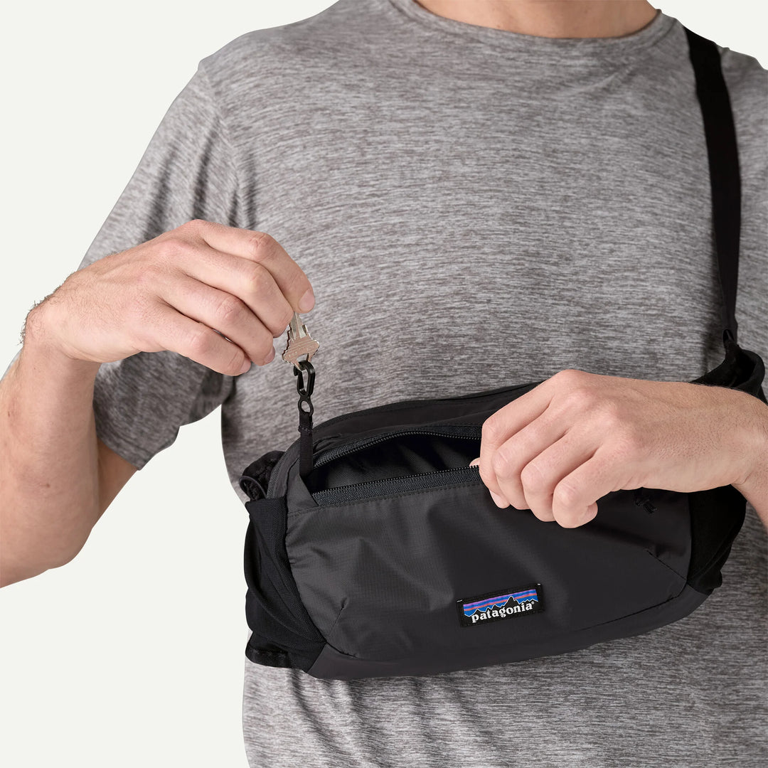 Person holding a black waist bag with Patagonia logo, wearing a gray shirt.