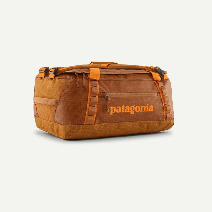 A Patagonia duffel bag in a warm brown and orange colorway, featuring the brand name in orange on the front, set against a light off-white background.
