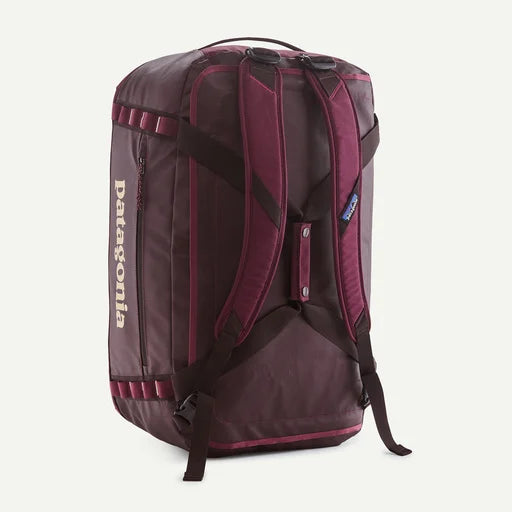 Patagonia backpack in a deep plum purple color with dark brown straps and trim, shown from a three-quarter back view against a light off-white background.