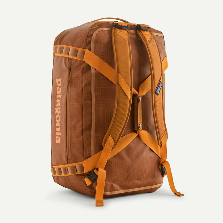 A brown Patagonia backpack shown from the back, featuring orange-brown padded shoulder straps, compression buckles, and a vertical Patagonia logo printed in orange on the side, set against a plain off-white background.