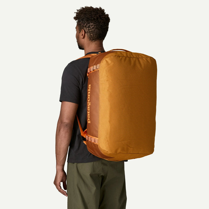 A man shown from the back wearing a large orange Patagonia duffel bag over his shoulders, photographed against a clean off-white studio background.