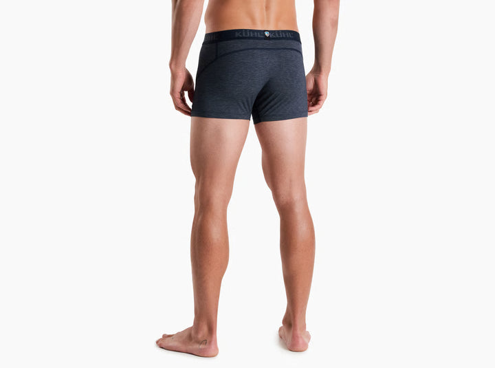 A man modeling dark gray heathered boxer briefs with a black waistband featuring the KUHL logo, shown against a plain white background.