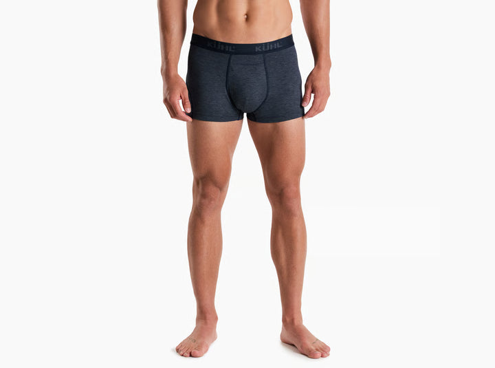 A man modeling dark gray heathered boxer briefs with a black waistband featuring the KUHL logo, shown against a plain white background.