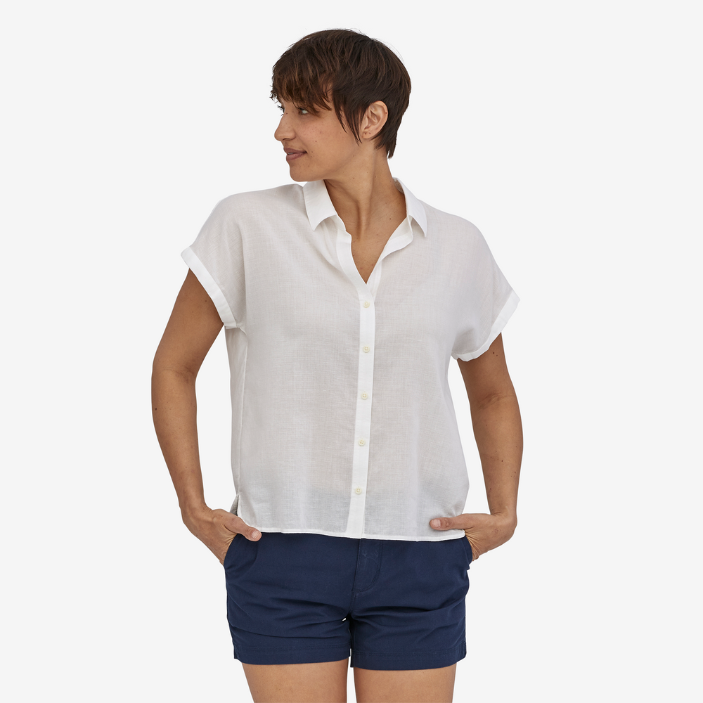 Woman wearing a white button up short-sleeve shirt and navy shorts on a white background