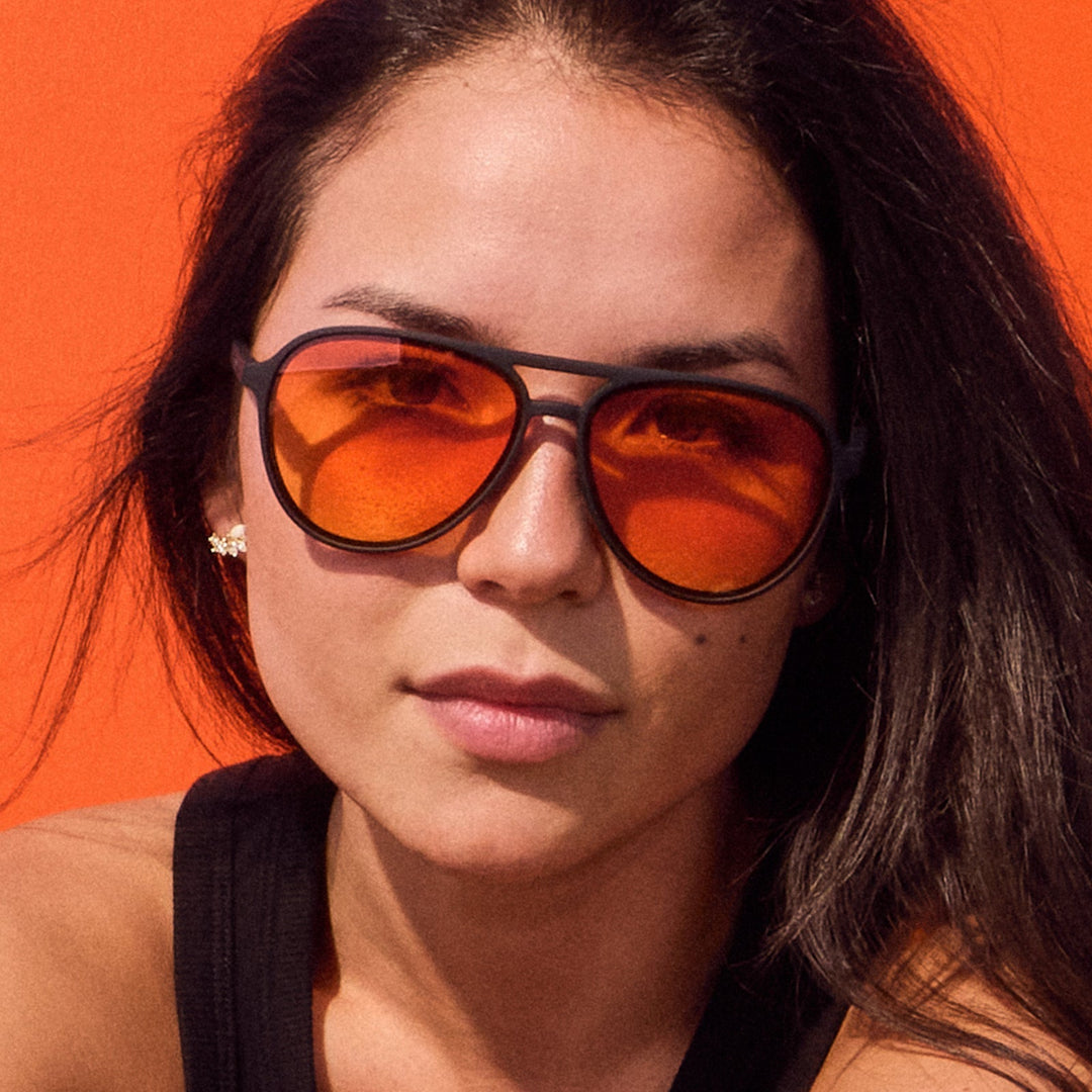 Woman wearing orange-tinted sunglasses against an orange background