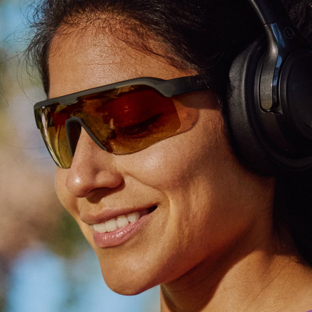 Woman wearing reflective sunglasses and large headphones with a blurred natural background
