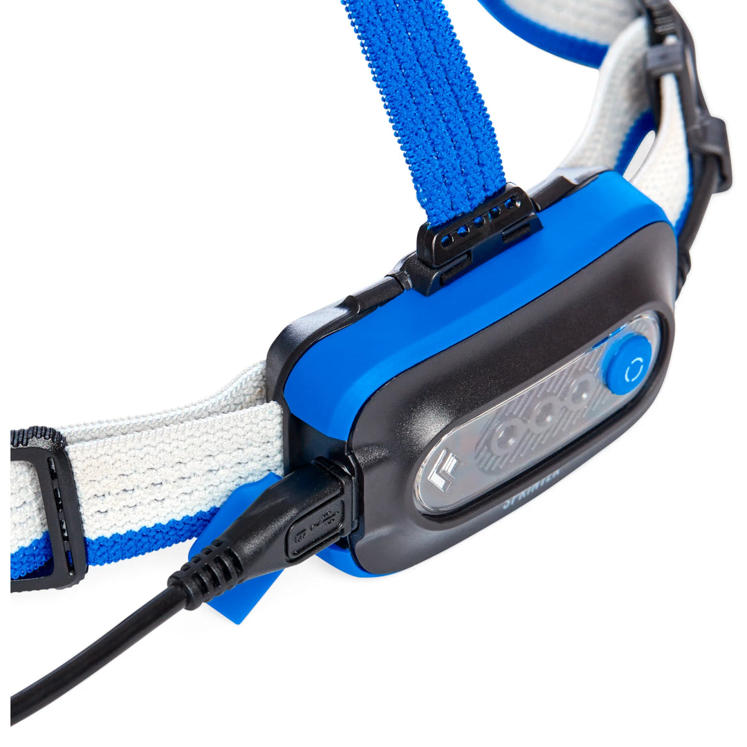 Close-up of a blue and black headlamp with white strap on a white background