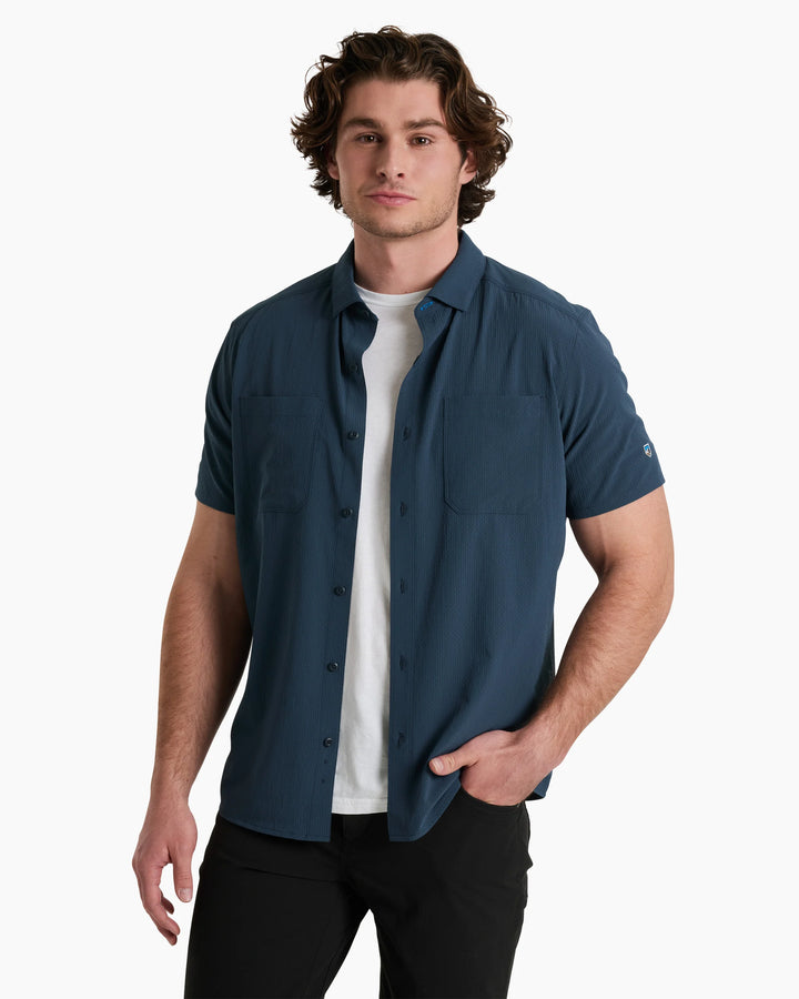 Man wearing a blue short-sleeve shirt over a white shirt on a white background
