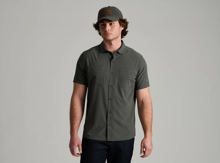 Man wearing a gray short-sleeve shirt and cap against a plain background