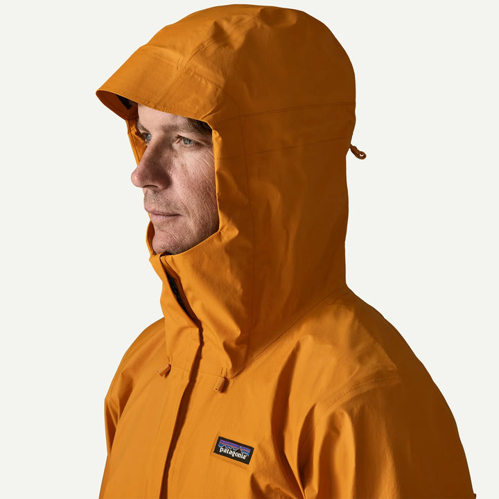 A man wearing a Patagonia hooded rain jacket in a warm orange-brown color, shown in profile against a light off-white background.