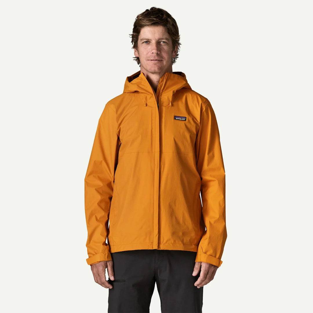 A man wearing a Patagonia hooded jacket in a vibrant orange color, paired with dark pants, standing against a solid off-white background.