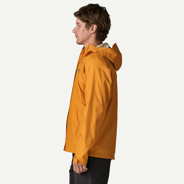 A man in profile wearing a bright mustard yellow hooded jacket against a clean off-white background.
