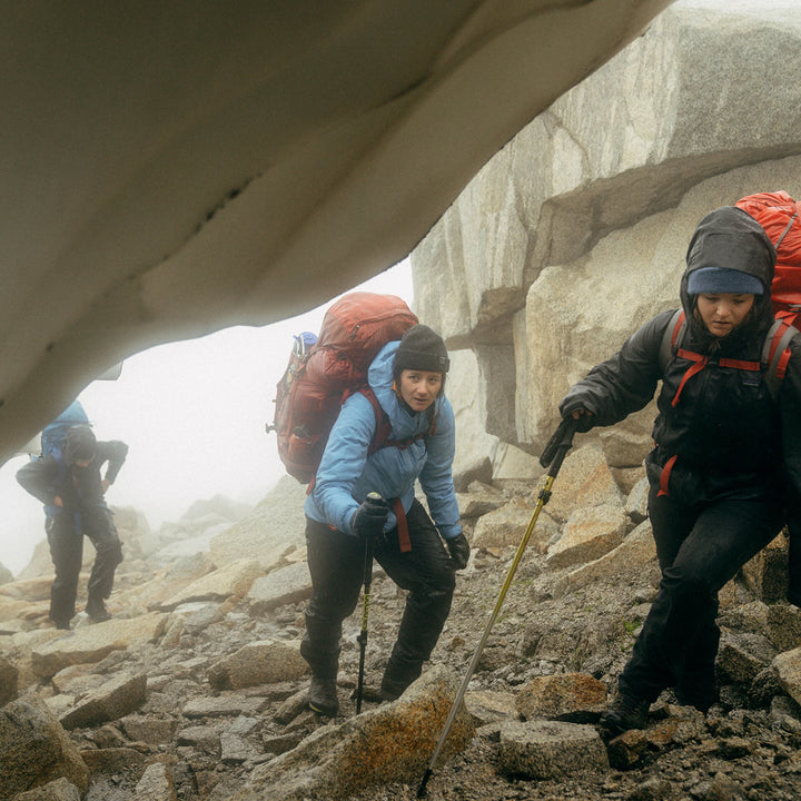 Hikers with backpacks and walking sticks climbing rocky mountain terrain.