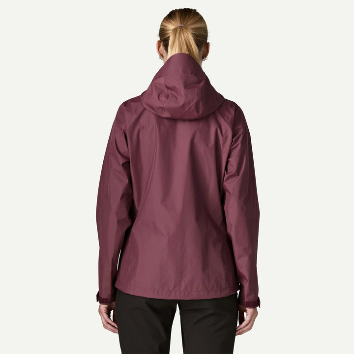 A woman viewed from the back wearing a hooded jacket in a muted burgundy or plum tone, paired with black pants, against a plain white studio background.