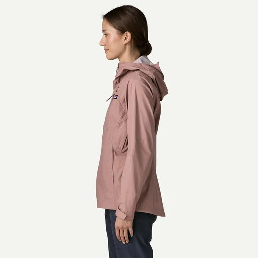 A woman shown in profile wearing a dusty rose hooded jacket and dark navy pants against a clean off-white background.