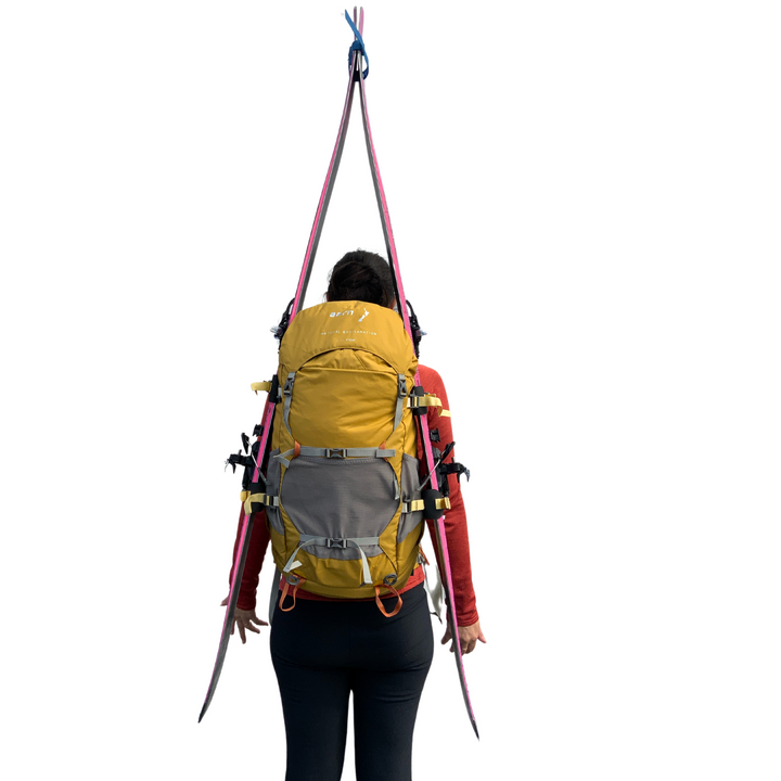 Person wearing an Aarn backpack with skis attached using yellow ski straps