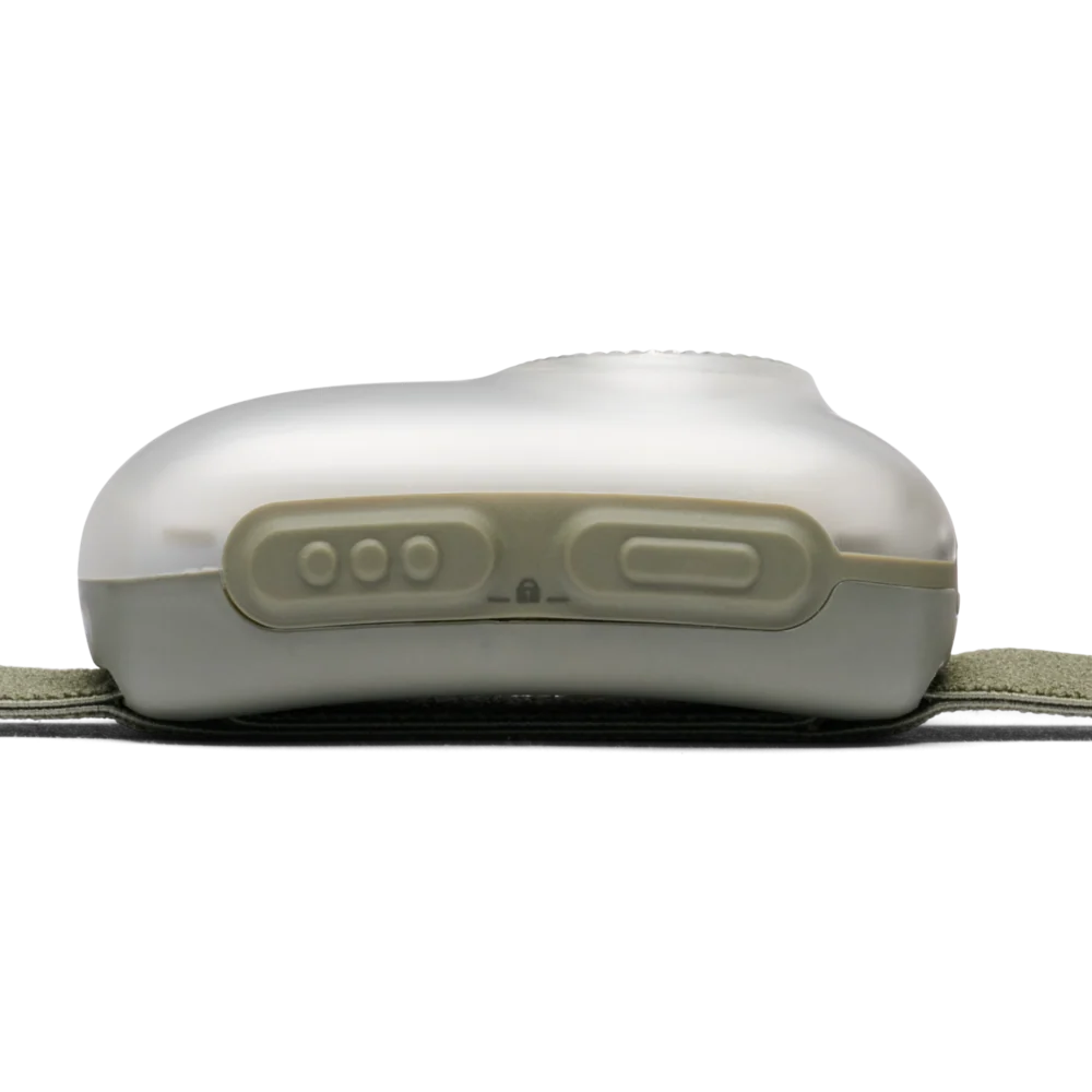 A close-up of a white electronic control unit with three round buttons and one larger rectangular button on a light gray surface, resting on a dark strap with an olive green fabric band visible at the sides.