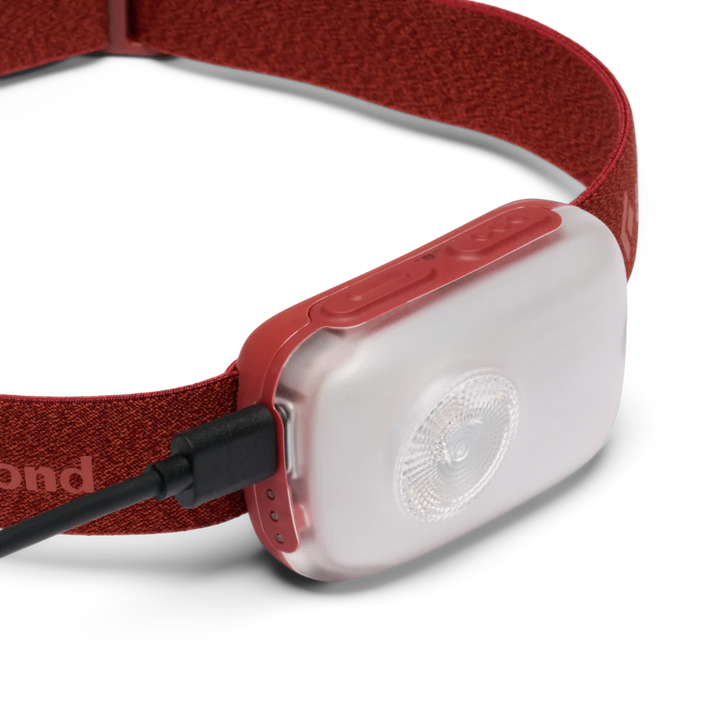 A close-up of a red headlamp with a translucent white light module and a black cable connector, shown on a clean white background.