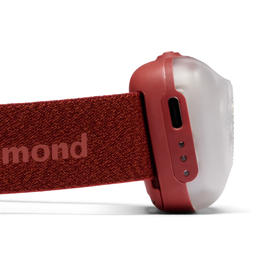 Close-up side view of a red headlamp with a textured fabric headband and a translucent white dome-shaped lamp housing, shown on a white background.