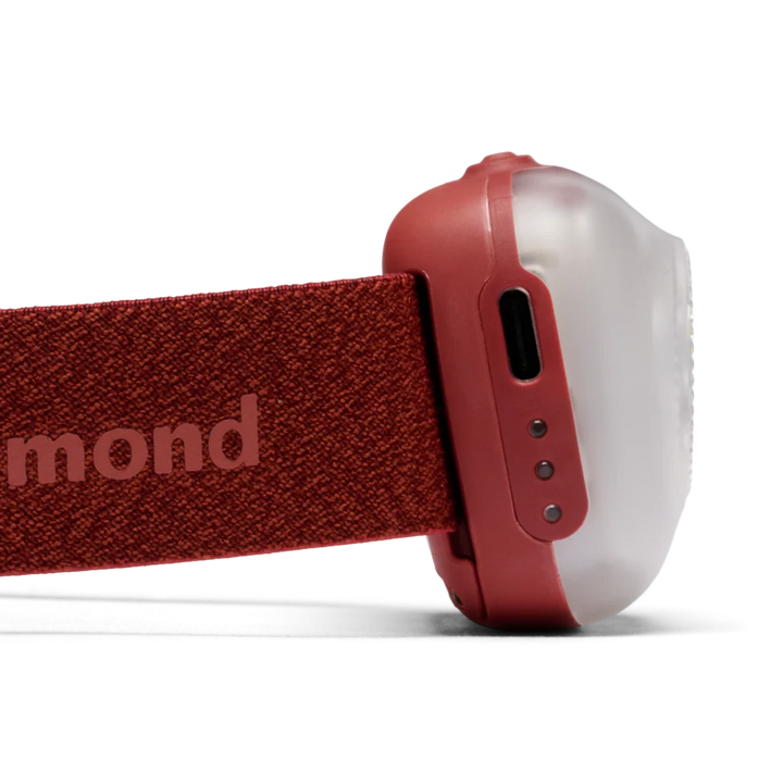 Close-up side view of a red headlamp with a textured fabric headband and a translucent white dome-shaped lamp housing, shown on a white background.