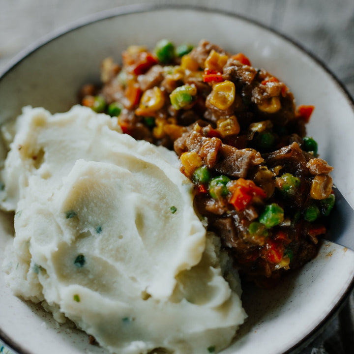 Mashed potatoes with a side of vegetable and meat dish on a plate.