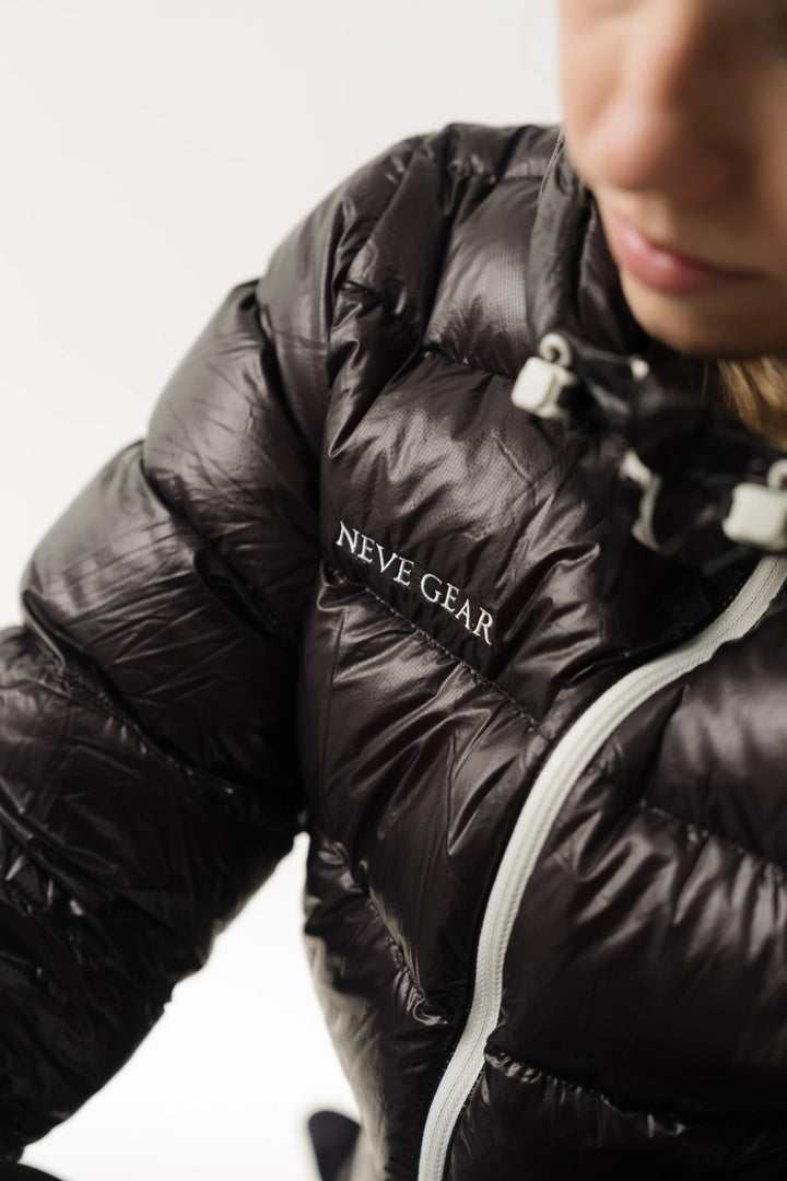 A close-up of a person wearing a shiny black puffer jacket with white zipper details and the brand name &