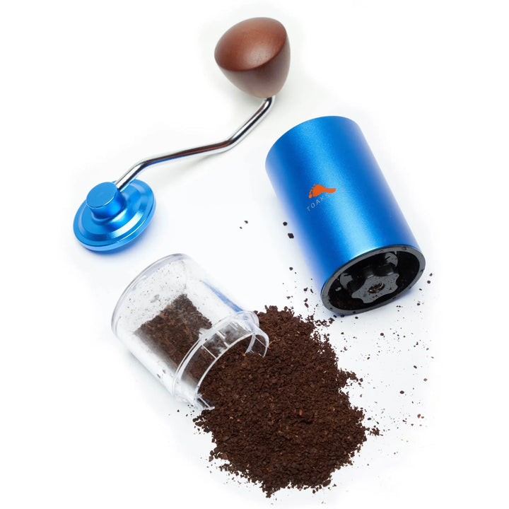 Blue metal hand coffee grinder disassembled on a white background with a spill of ground coffee