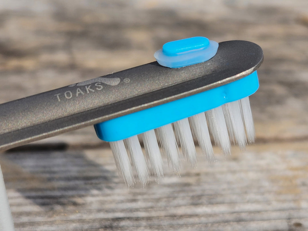 Close up of a blue toothbrush head clipped onto the handle of a metal hiking spoon