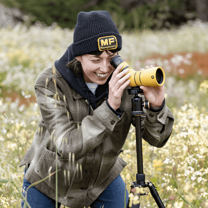 Person using a yellow spotting scope on a tripod in a natural setting