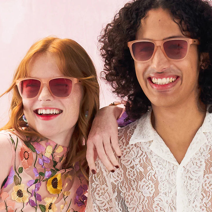 Two people wearing sunglasses with a pink background