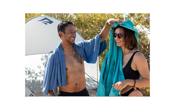 Two people using beach towels outdoors with a tent in the background