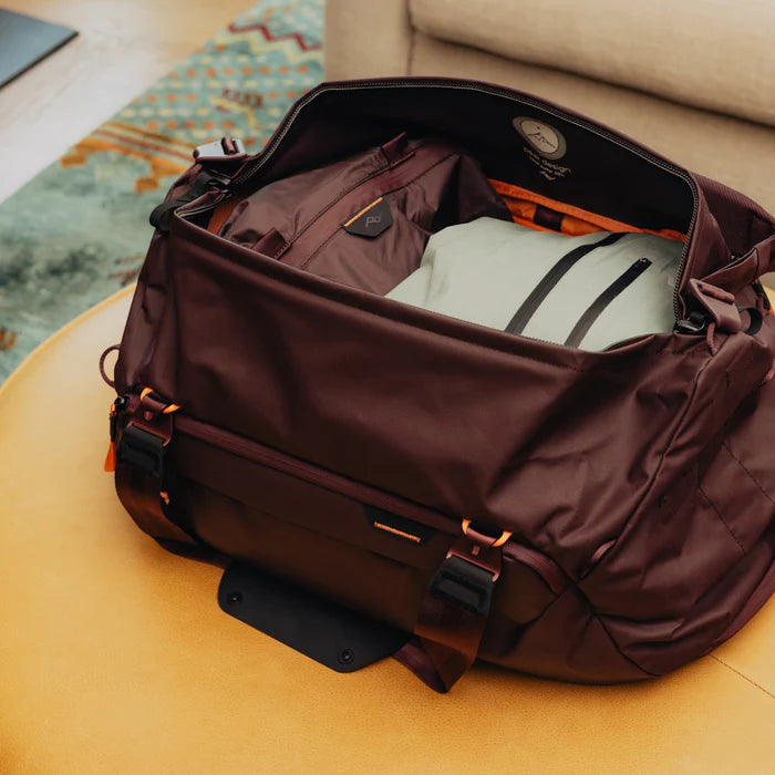 Brown duffel bag with clothes on a beige surface