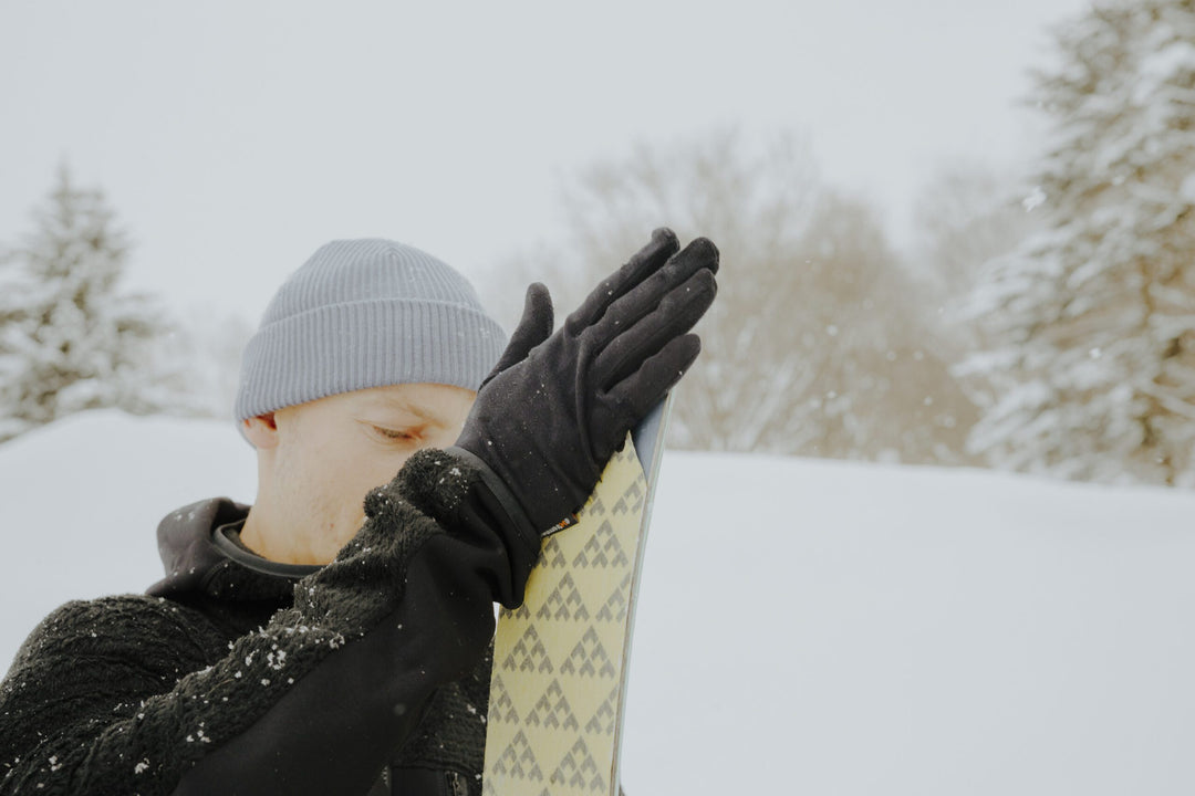 Person in winter clothing holding a ski with snow-covered trees in the background