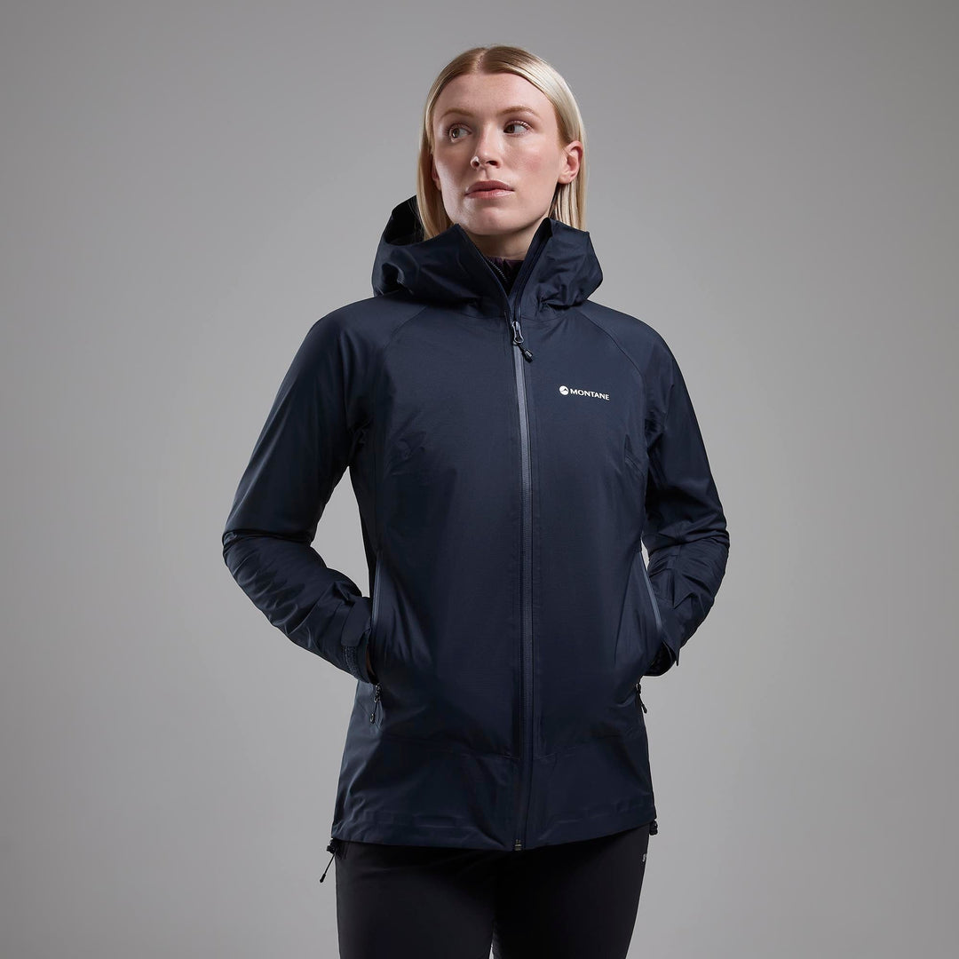 Woman wearing a dark blue raincoat with the Montane logo, hands in high pockets