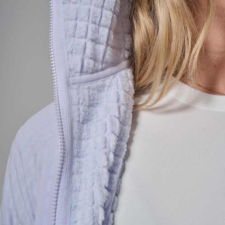 Close-up of a person wearing a light lavender fleece-lined zip-up jacket over a white top, showing the soft textured fabric and zipper detail.