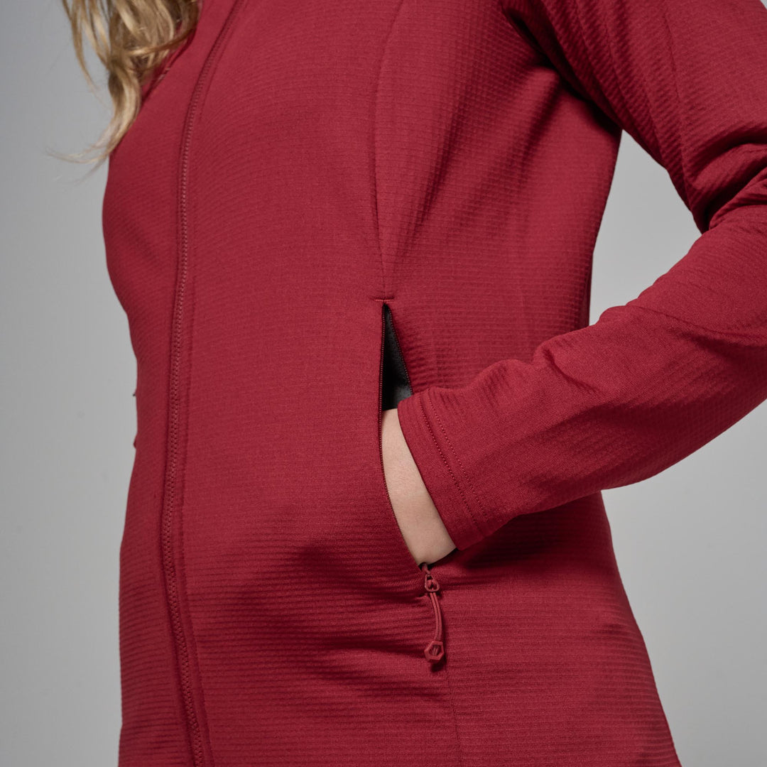 A close-up of a woman wearing a textured, deep red zip-up jacket, showing a side pocket with her hand inside, against a solid gray background.