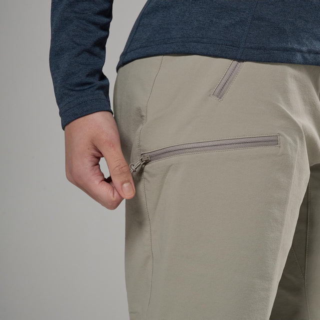 Person wearing beige pants with a zipper pocket on a plain background