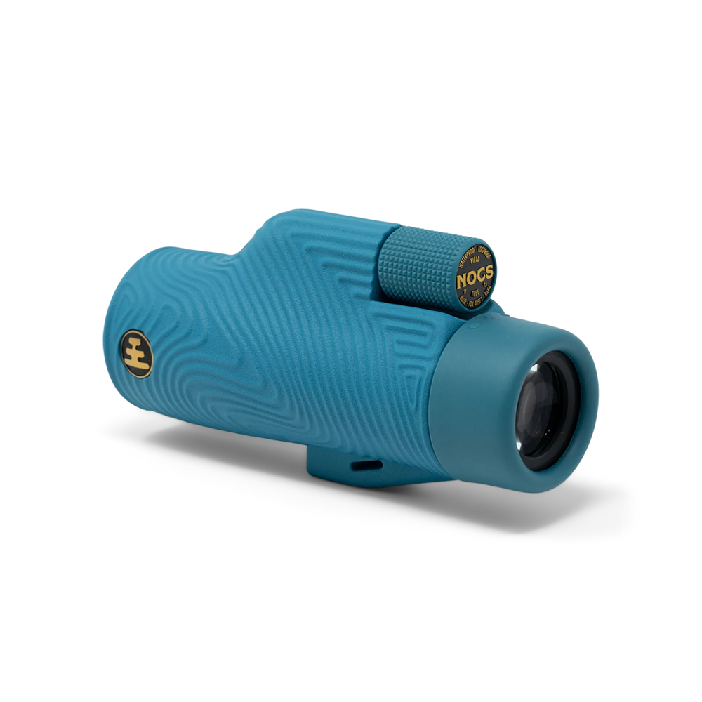 A teal blue monocular with a textured wavy pattern and gold accents, including a visible 'NOCS' logo on the focusing ring, shown on a clean white background.