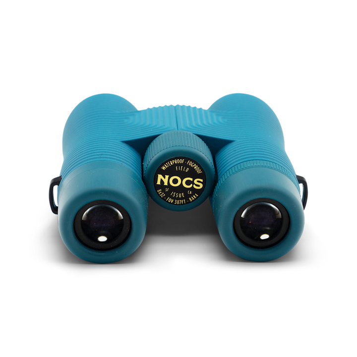Compact blue binoculars with Nocs Provisions logo on a white background, viewed from the eye piece end.