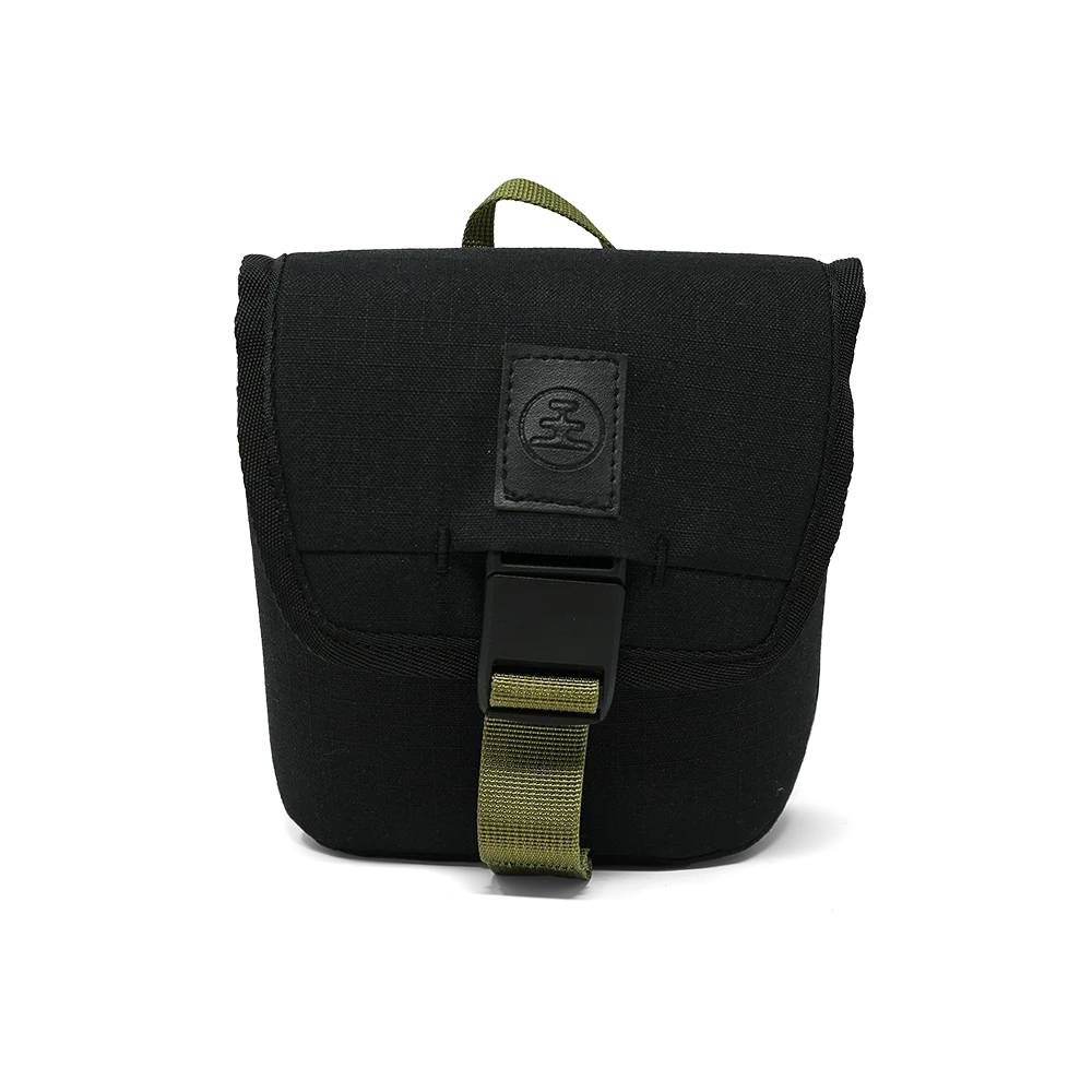 A black canvas utility pouch with an olive green webbing strap and a black plastic buckle, featuring a black leather patch with a circular logo on the front flap.