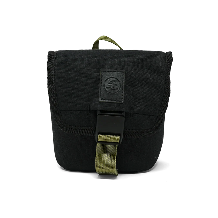 A black canvas utility pouch with an olive green webbing strap and a black plastic buckle, featuring a black leather patch with a circular logo on the front flap.