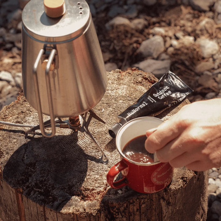 Person preparing coffee using a portable stove and coffee package on a natural background