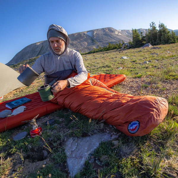 Man sitting on a sleeping pad outdoors with mountains in the background